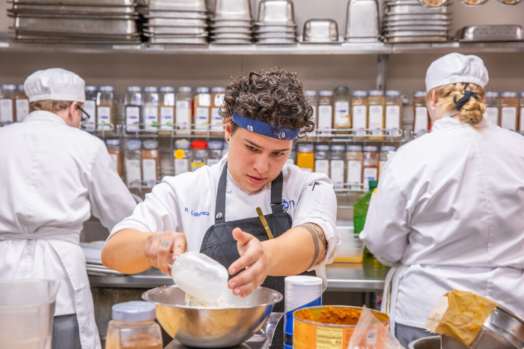 Person in chef white measuring flour on a scale.