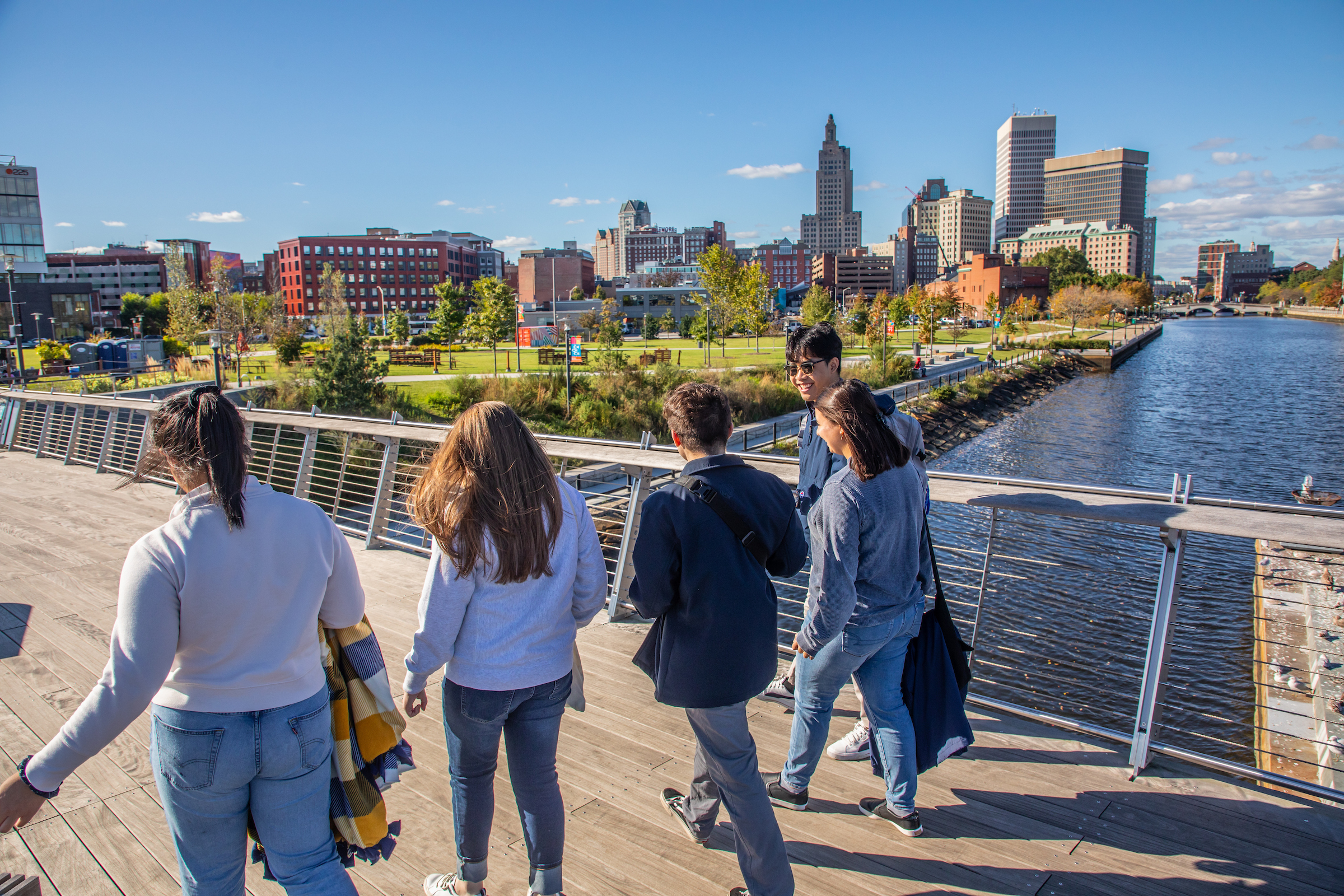 Fall 2023 Student Life in the City of Providence: Featuring Jason (Jae) Griener ’23 (cybersecurity), Lucia Manzo '25, Angela Savoca, and Sunny Sysomphou ’27 (Advertising) at the Pedestrian Bridge overlooking the Providence skyline.