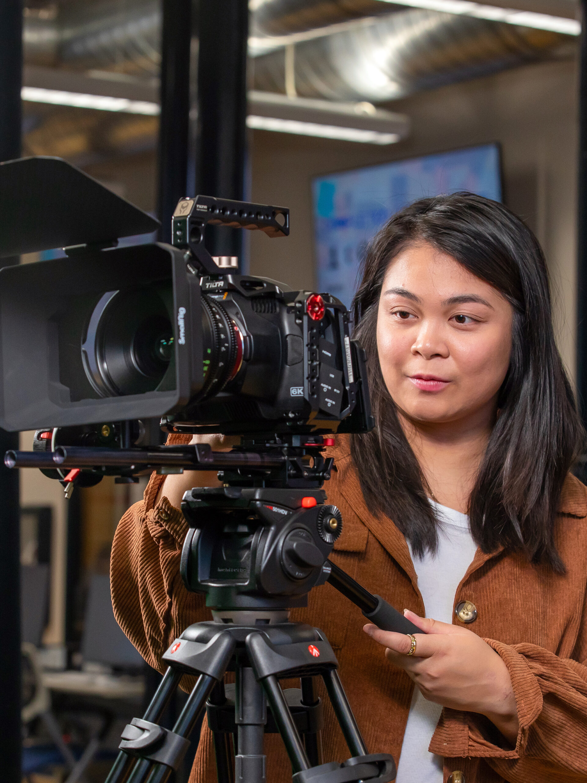 A person operates a professional video camera mounted on a tripod in a studio setting.