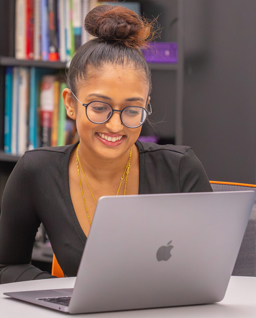 A person smiles while using a laptop in a library setting