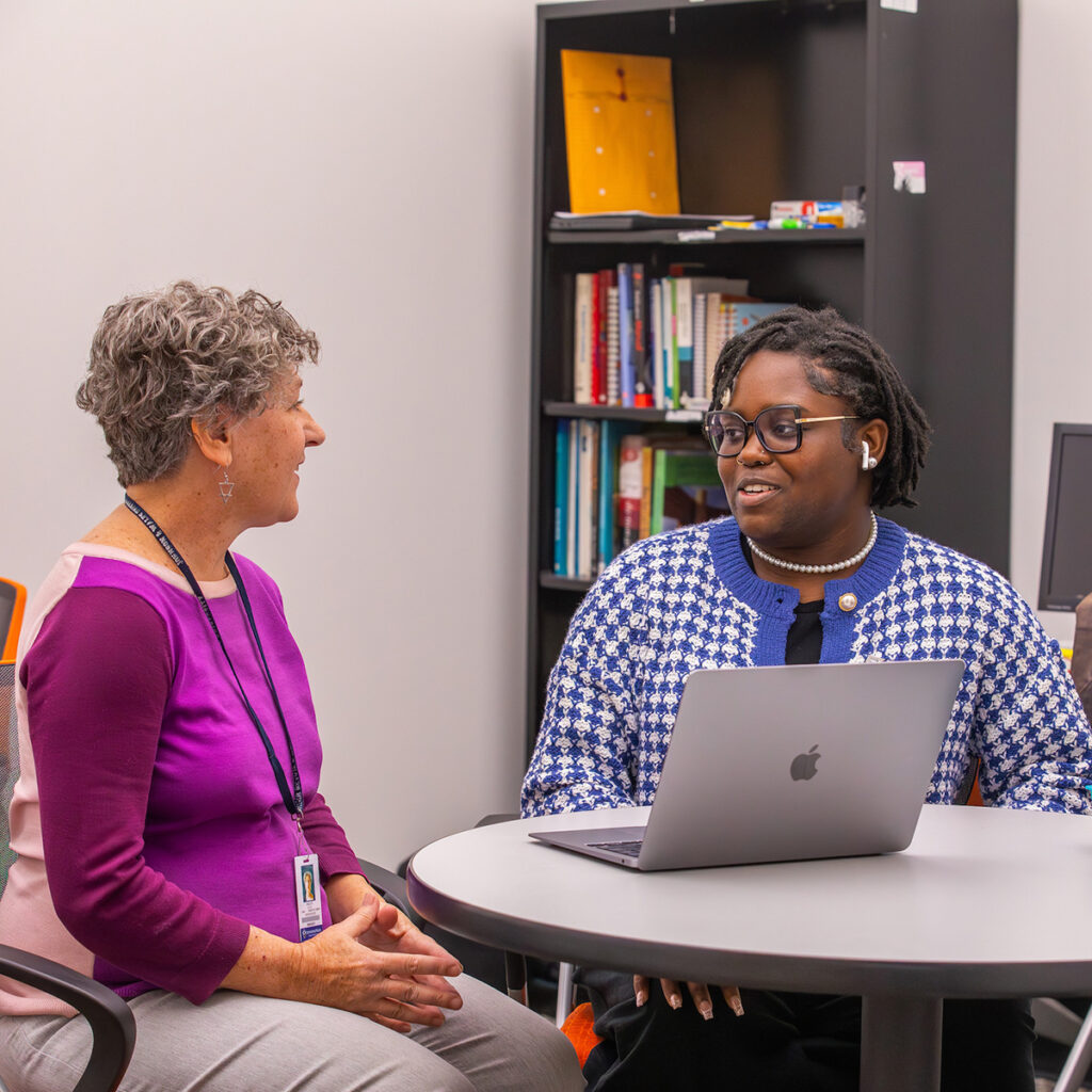 A student sites with an advisor at a table with a laptop.