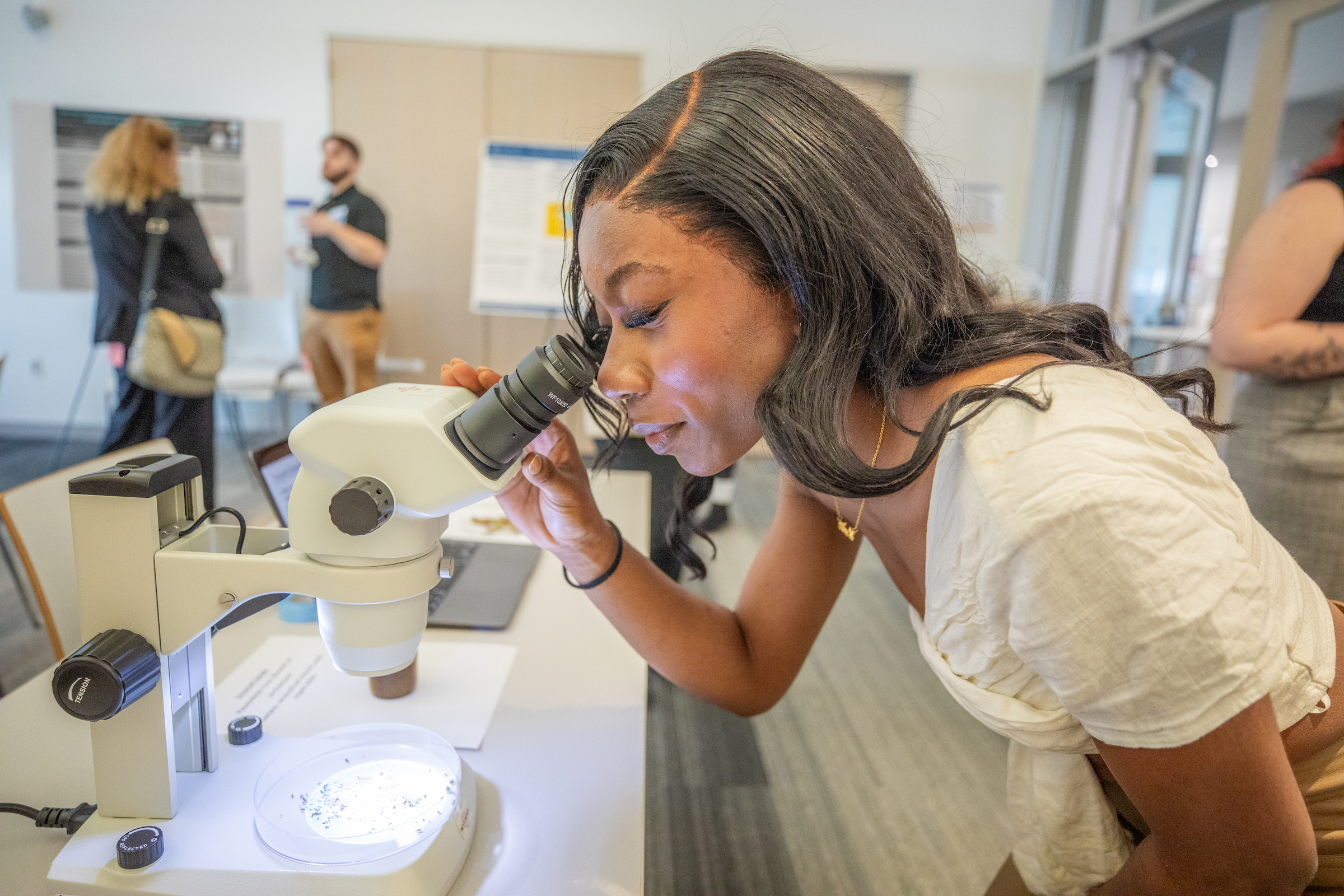 A person leans over a microscope, examining a specimen in a bright, modern laboratory setting.