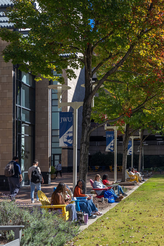Students relax in colorful chairs under autumn trees on the campus lawn.
