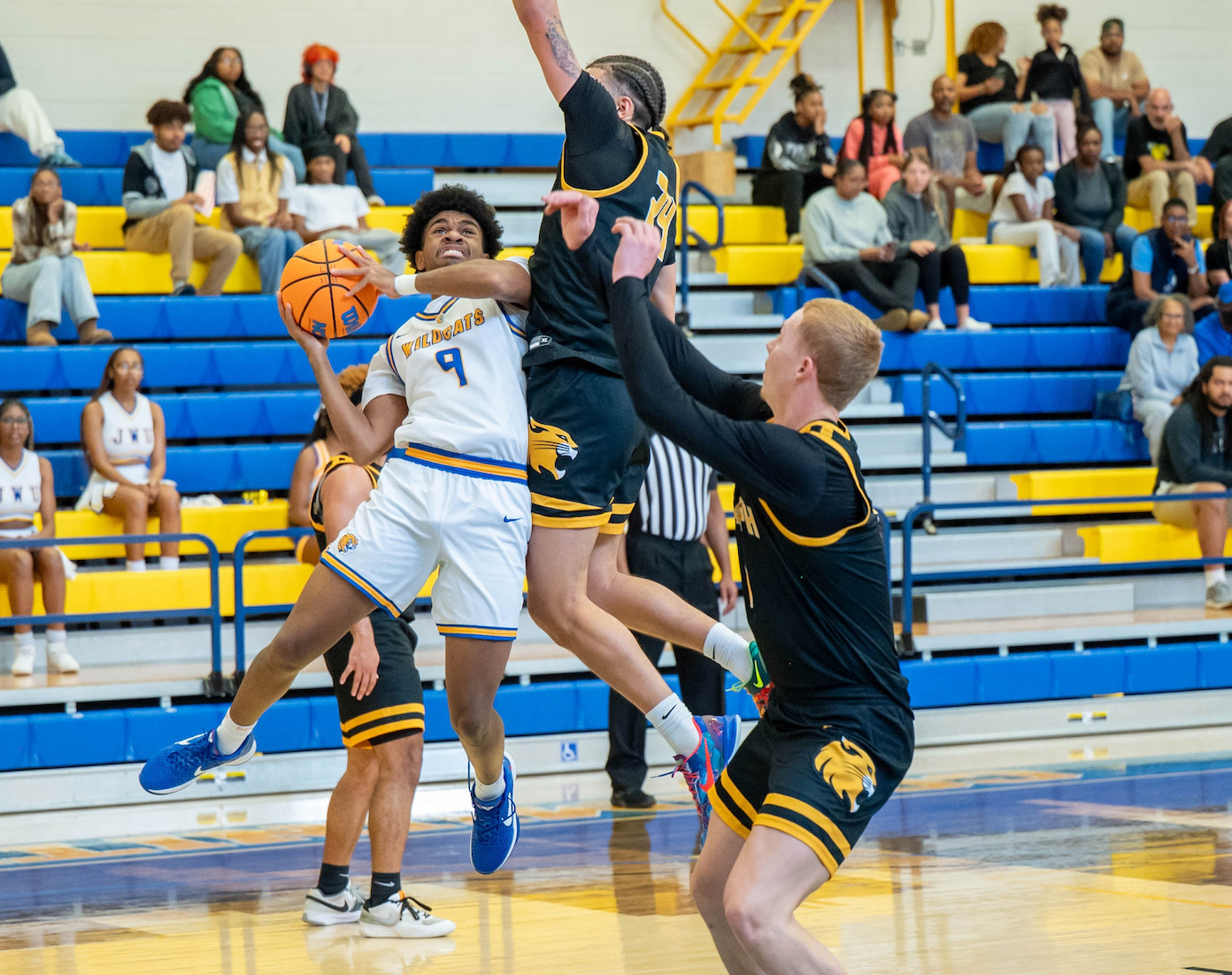 A basketball player in a white uniform shoots the ball while being defended by opponents in black uniforms during a game.