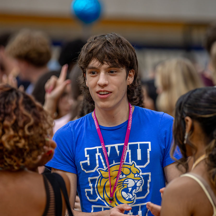 A student in a blue Johnson and Wales University t-shirt engages in conversation with others at orientation.