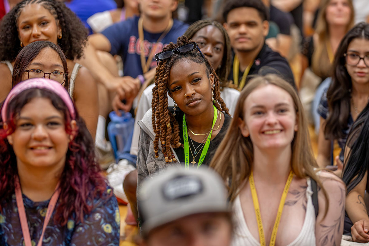 A group of students sit attentively in a group at orientation in the Wildcat Center gymnasium.