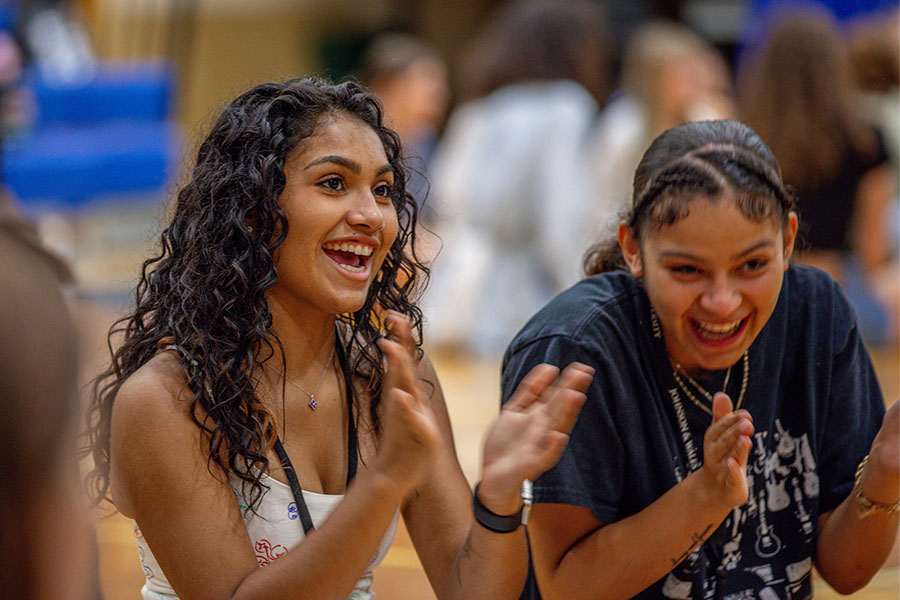 Two students are clapping and smiling enthusiastically in the Wildcat Center during orientation.
