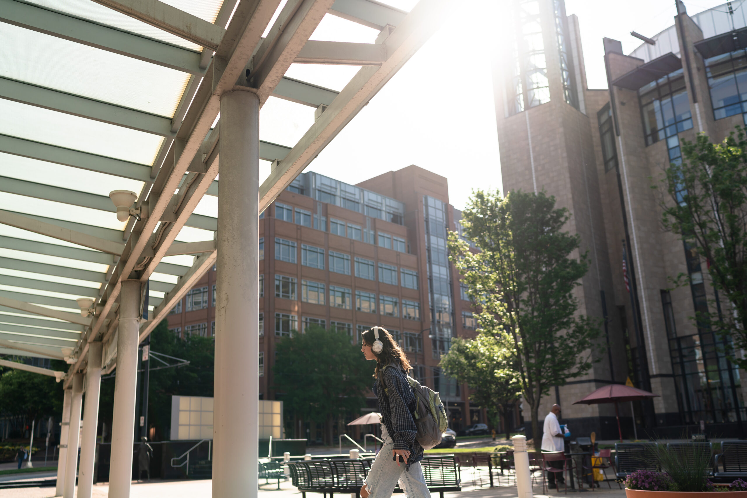 Modern city walkway with white columns, benches and people passing through.