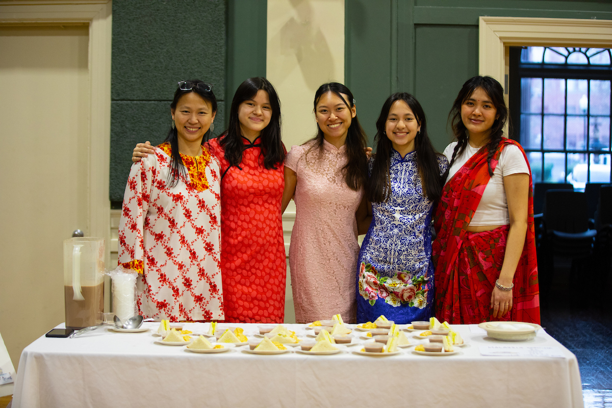 Five individuals stand together behind a table displaying assorted pastries and beverages, smiling for the camera.