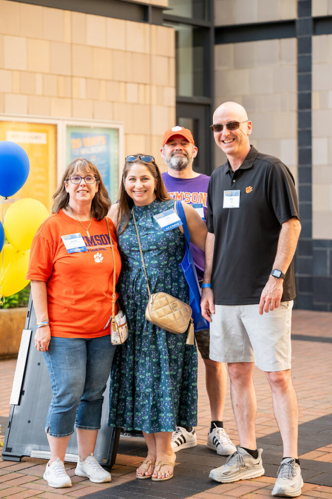 Four people dressed in Clemson Tigers apparel pose together outdoors at an event, smiling for the camera.