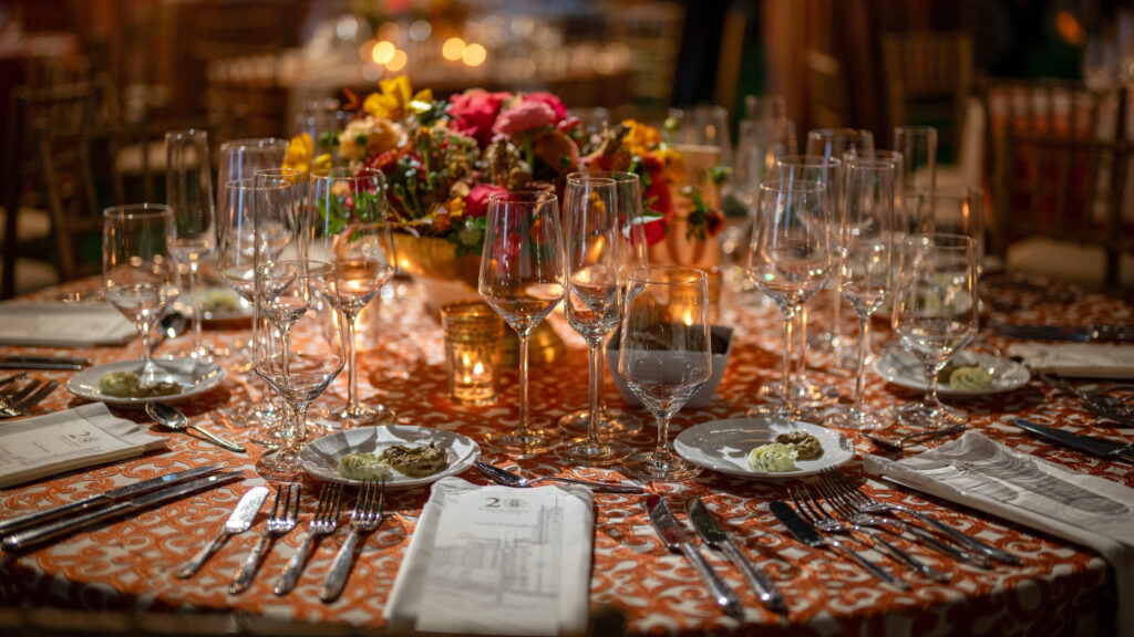An elegantly set dining table with glassware, plates, and a vibrant floral centerpiece under warm ambient lighting.