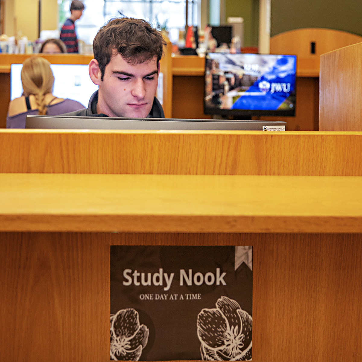 A student looking at a computer in a private booth in the library, with a sign reading "Study Nook: One Day at a Time."