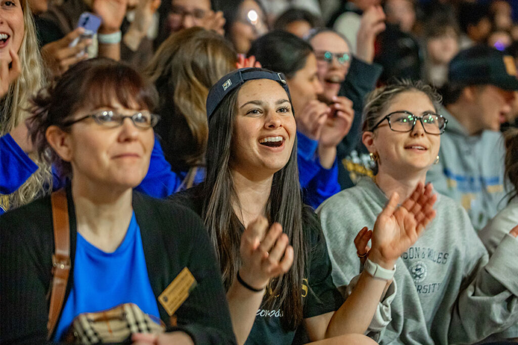 A group of students at a pep rally, clapping and smiling.