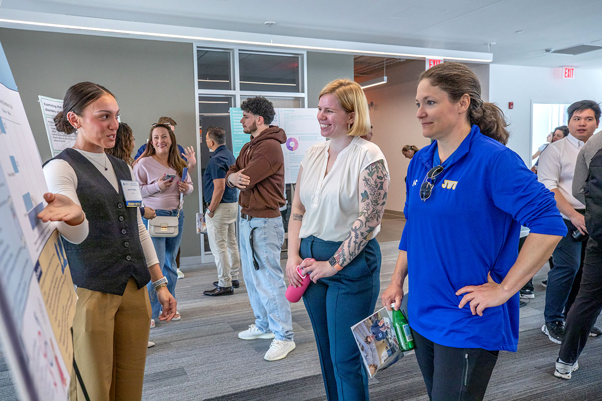 A student presents her project to two observers at the Student Research and Design Symposium.