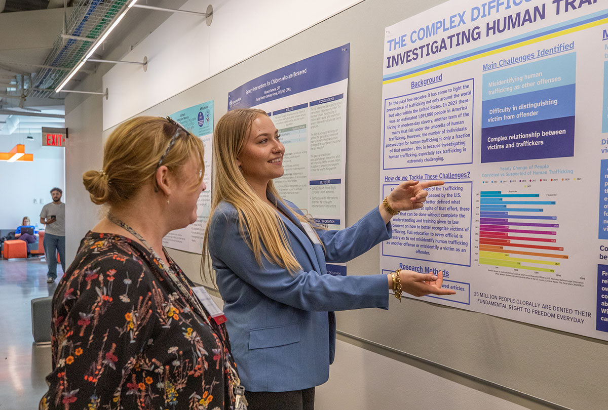 A student discussing her project with an attendee while examining a research poster.