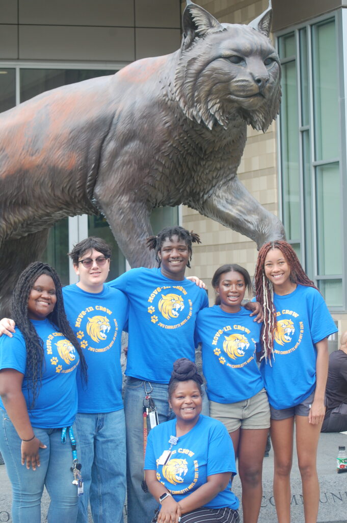 A group of students wearing matching blue "Move-In Crew" shirts poses in front of a large statue of a bobcat.