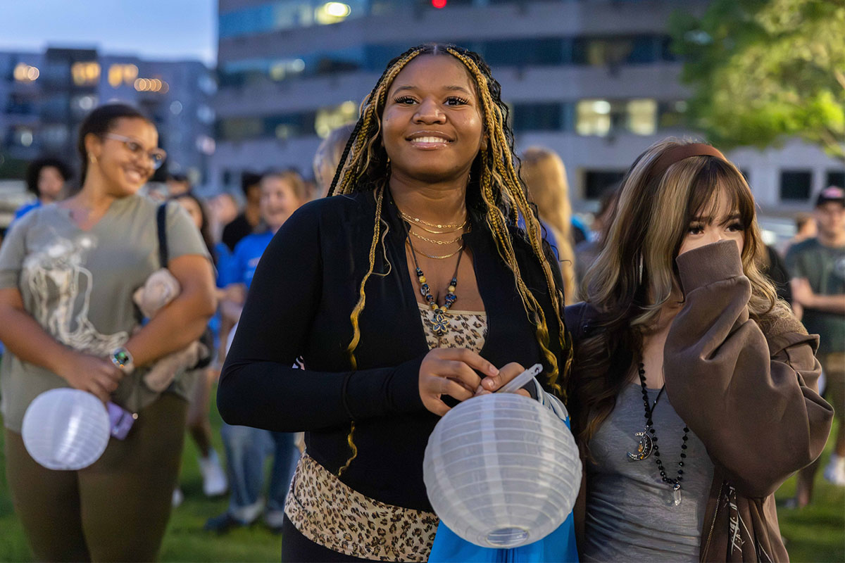 A group of students outdoors at dusk, smiling and holding paper lanterns to hang.