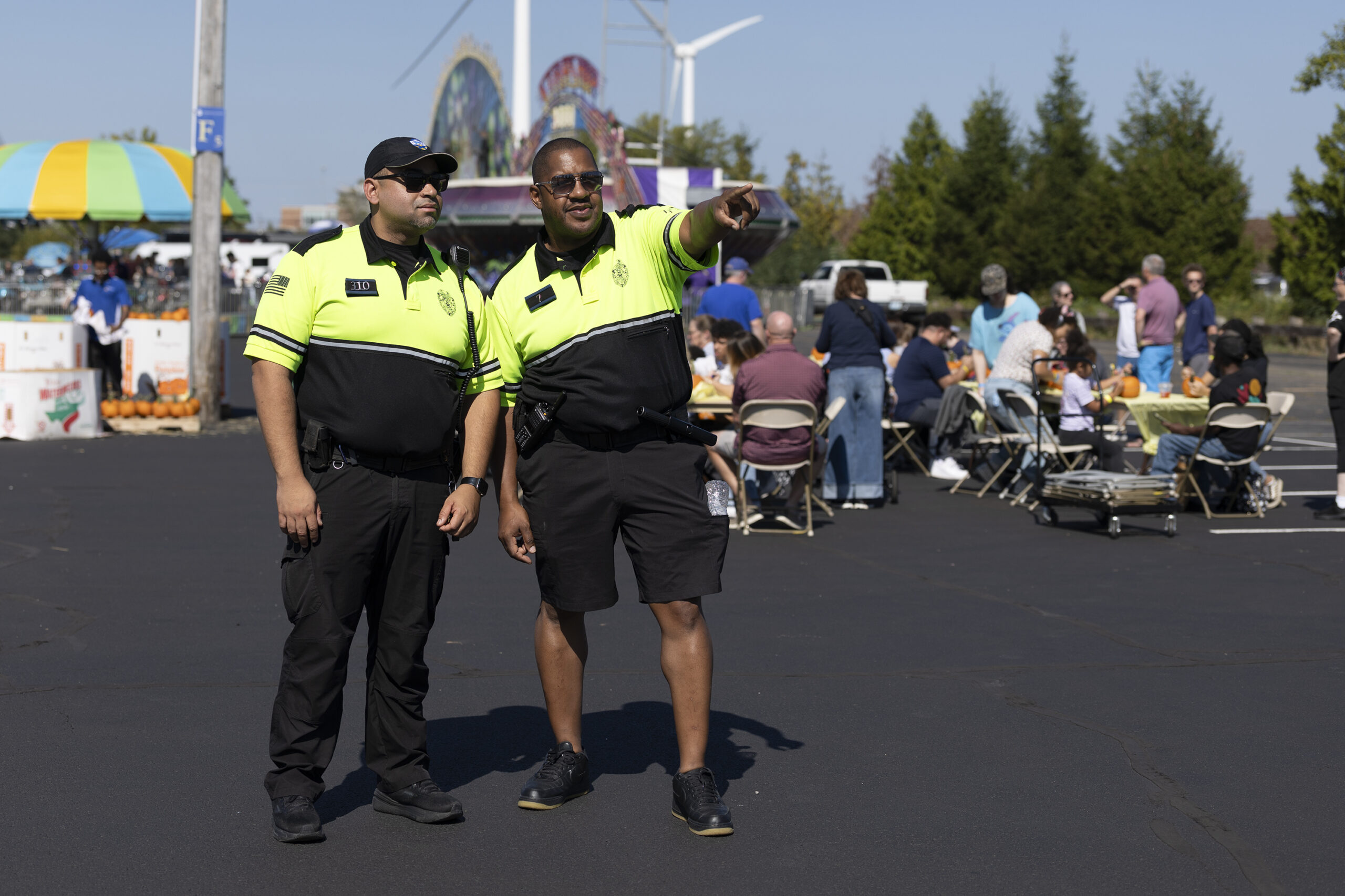 Two campus safety officers stand at an outdoor event while one points across the crowd.