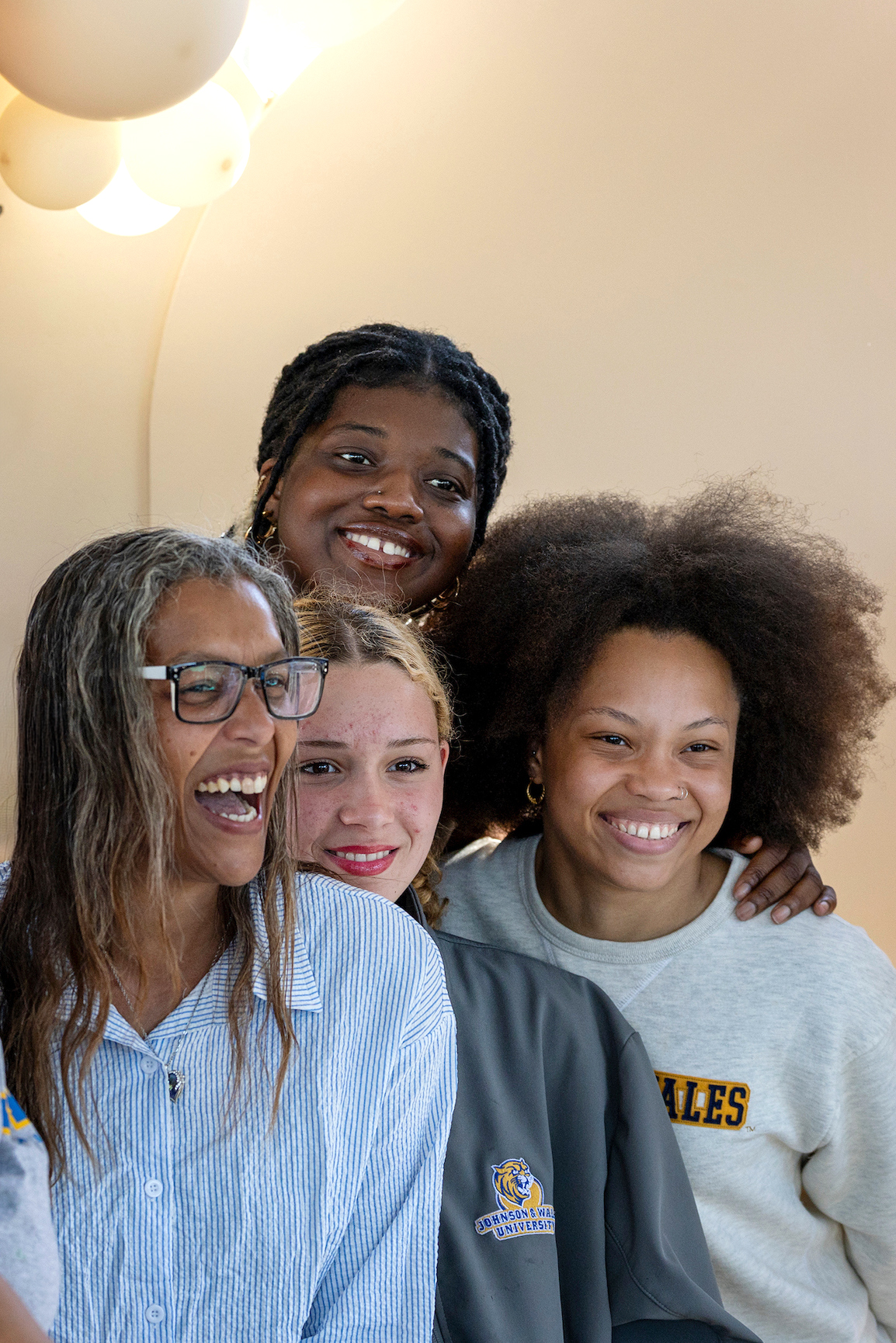 A group of five people smile together at a "Family Weekend 2025" event, with colorful balloons and a festive backdrop.