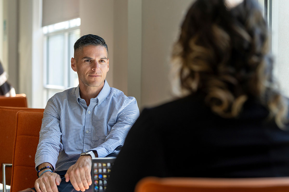 A graduate student sits facing an advisor in an office setting.