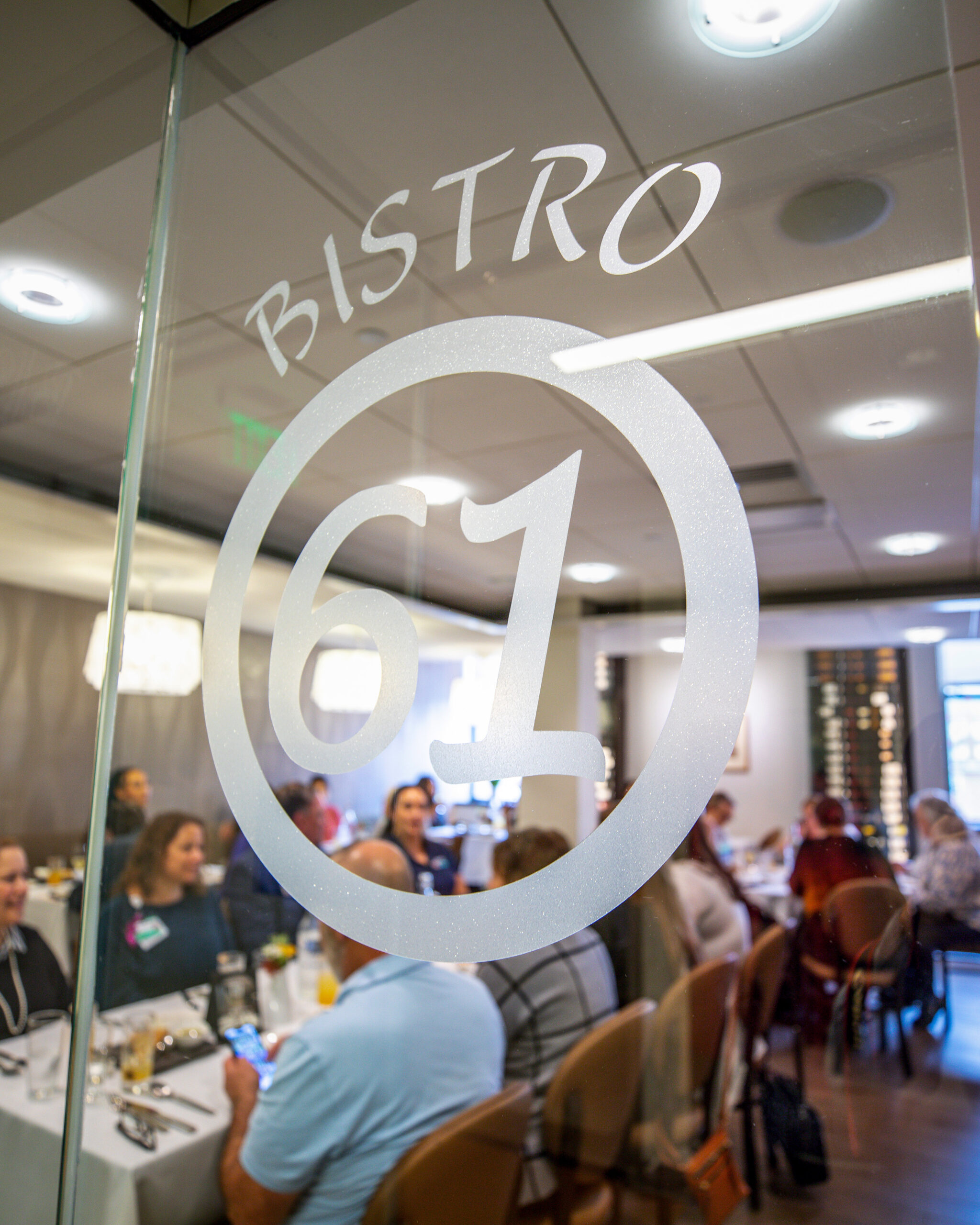Guests dine inside Bistro 61 as seen through the glass entrance with the restaurant logo.