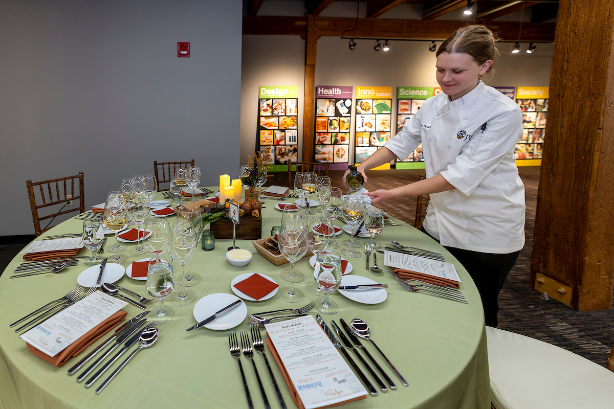 A chef prepares a table setting by pouring liquid into a glass at a formally arranged dining table.