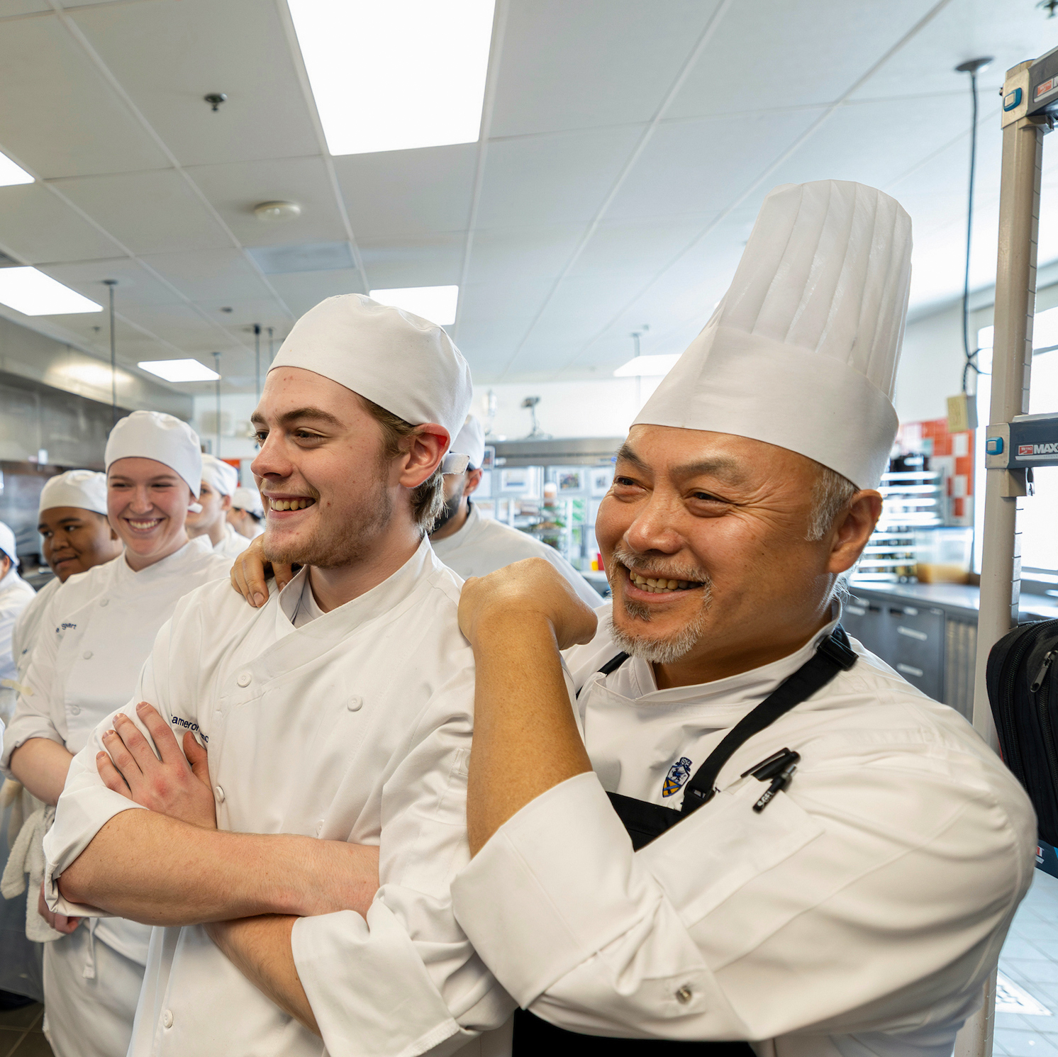 A group of chefs in a professional kitchen, smiling and interacting with one another.