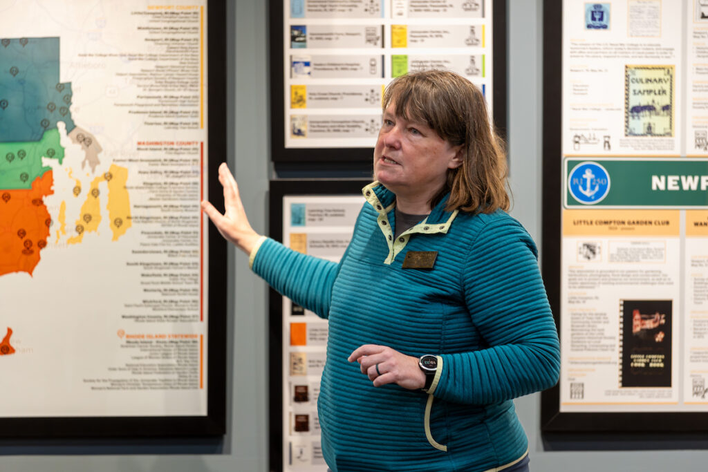 A person gestures toward a colorful map displayed on a wall, surrounded by informational posters.