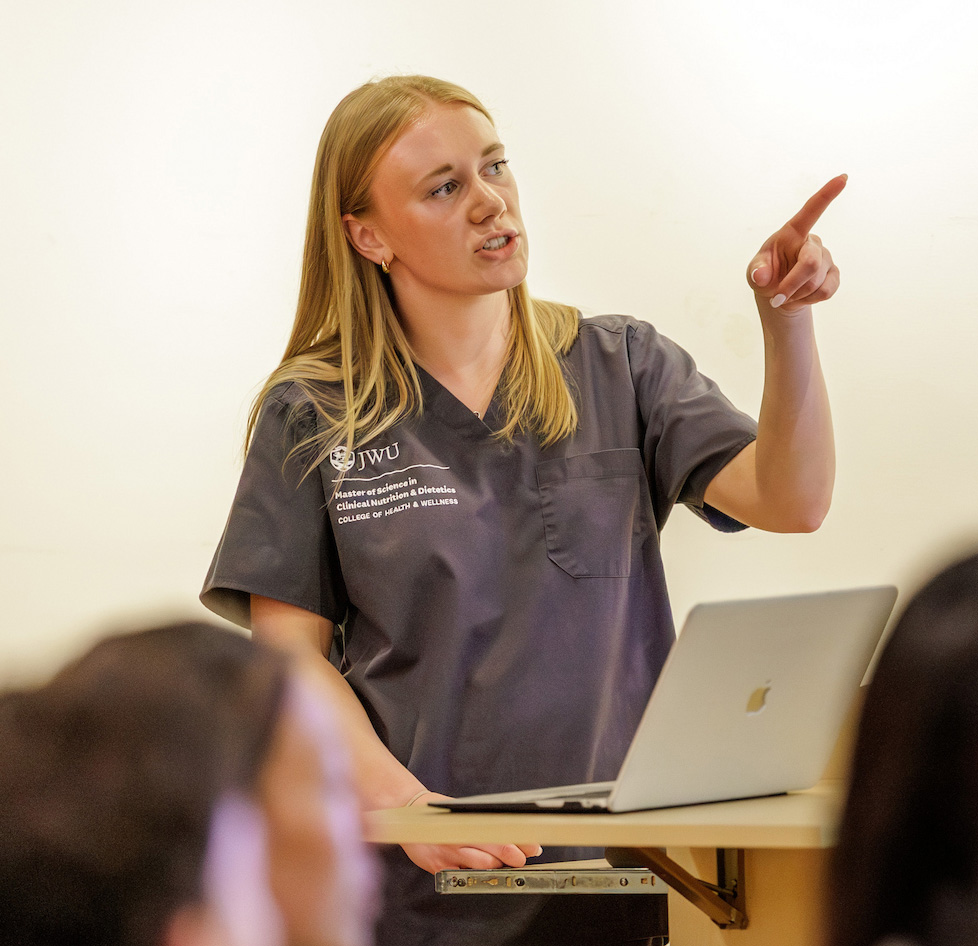 A graduate student points toward a screen in front of an audience while presenting