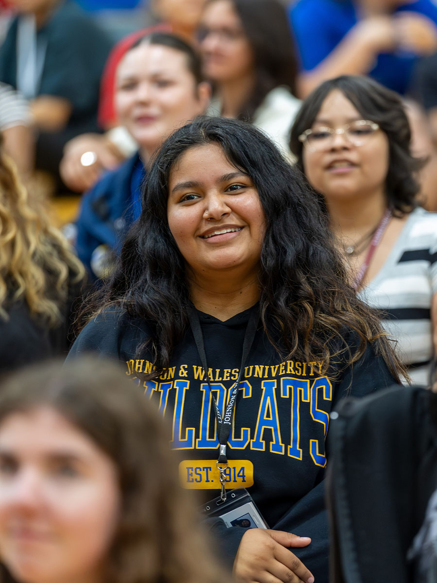 A student wearing a Wildcats sweatshirt, smiling, sitting with a group of students at orientation.
