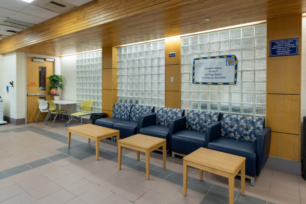A modern waiting area with blue upholstered sofas, wooden tables, and glass block walls, featuring a sign indicating it's a student room.