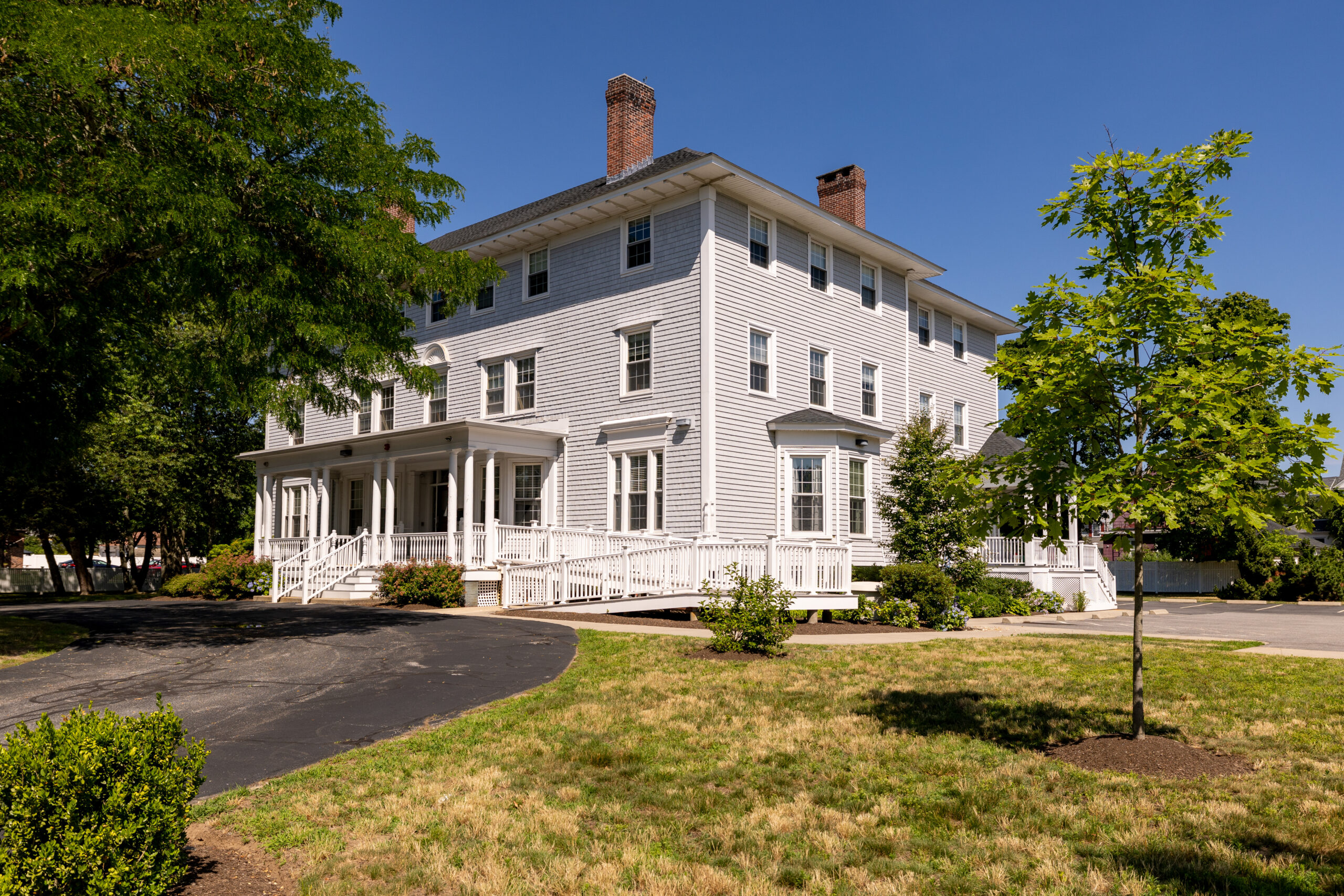 A gray house with white trim with grass and trees.