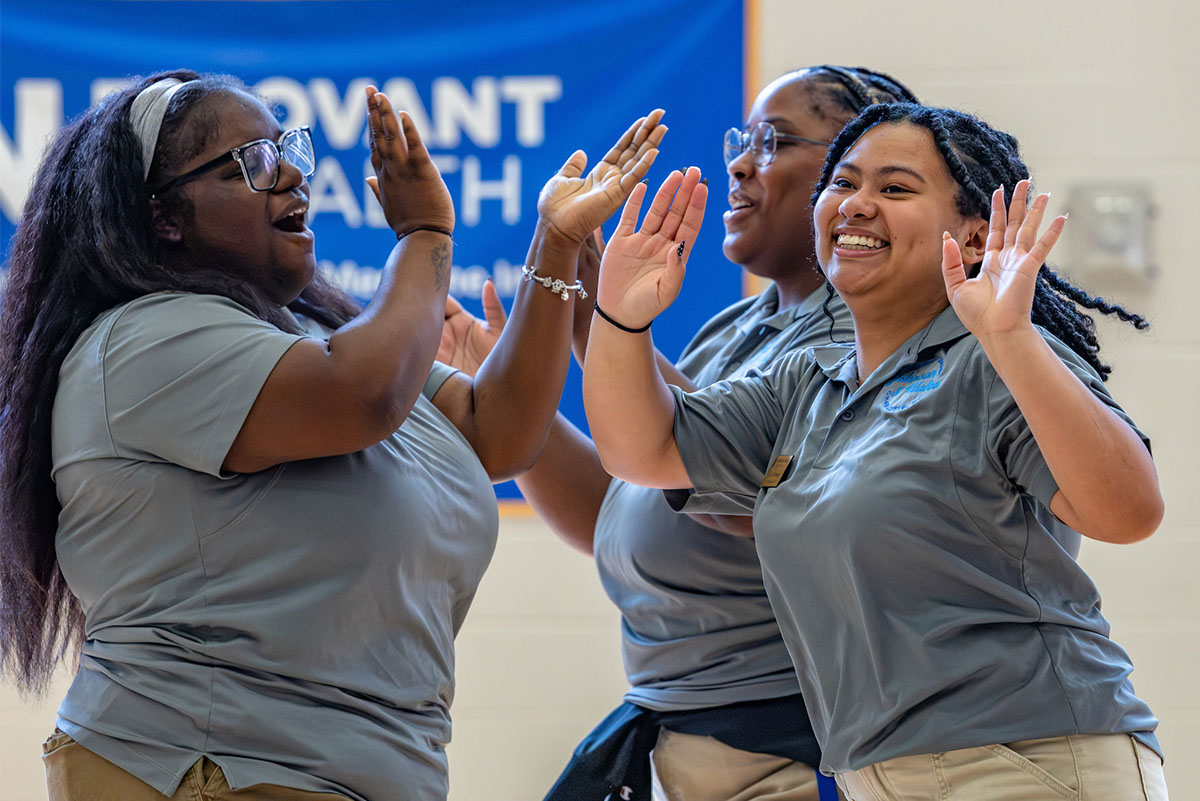 Three cat team members in matching uniforms joyfully high-five each other in a gymnasium.
