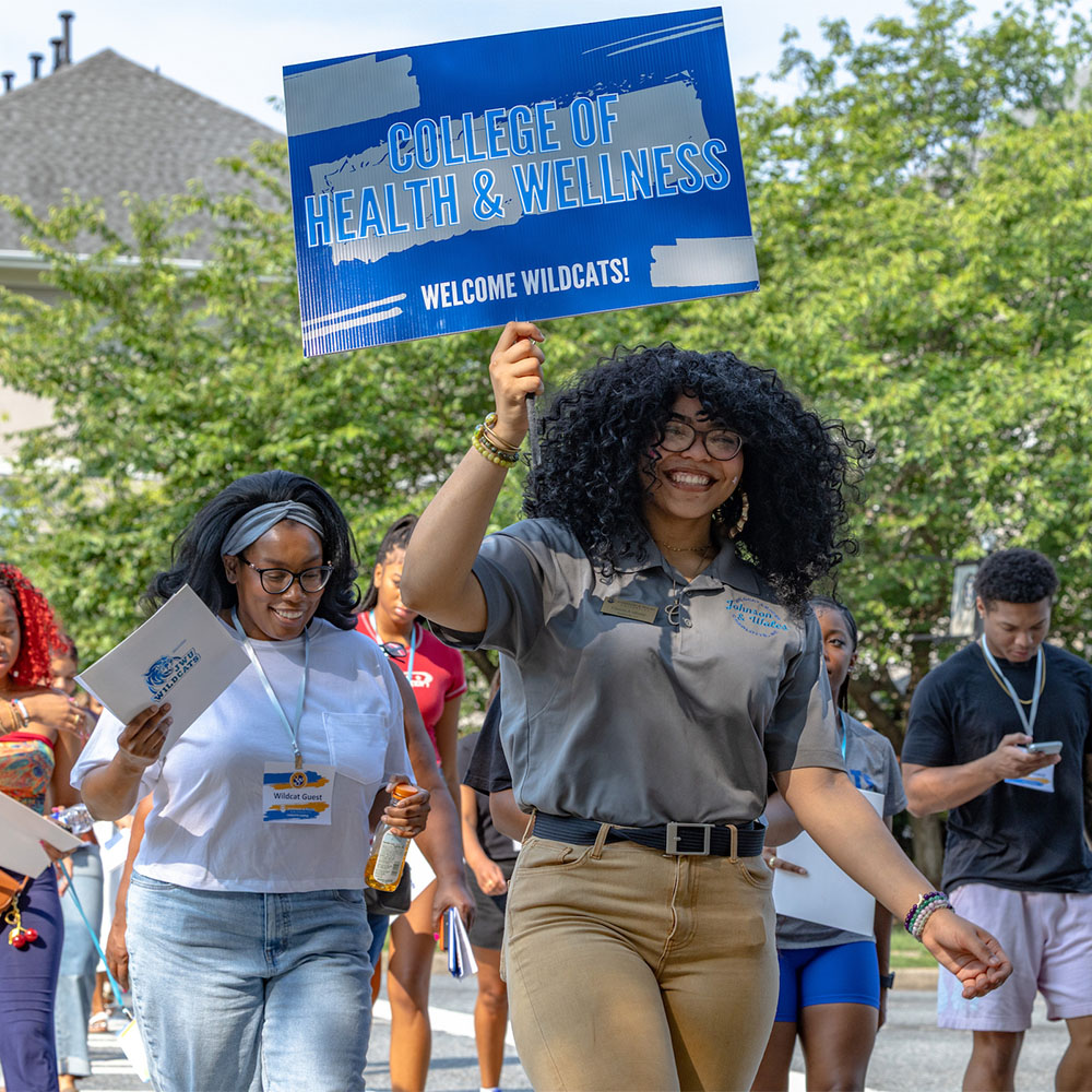 A member of the cat team holds a sign welcoming new students to the College of Health and Wellness.