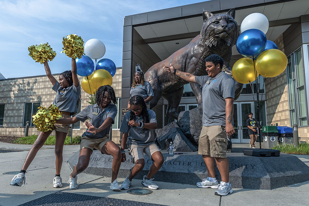 Members of the cat team dance in front of the Wildcat statue,  surrounded by blue, white and gold balloons.
