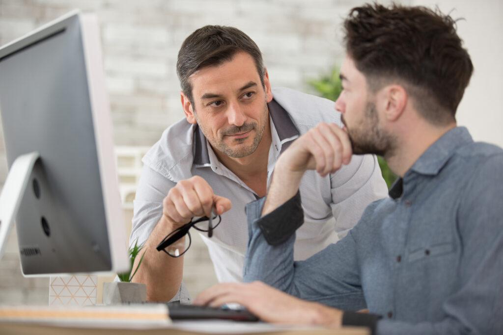 Two persons talking over a computer and papers.