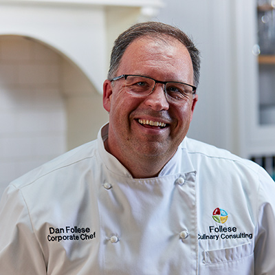 Portrait of Dan Folese, corporate chef and culinary consulting professional, smiling while wearing a white chef’s coat.