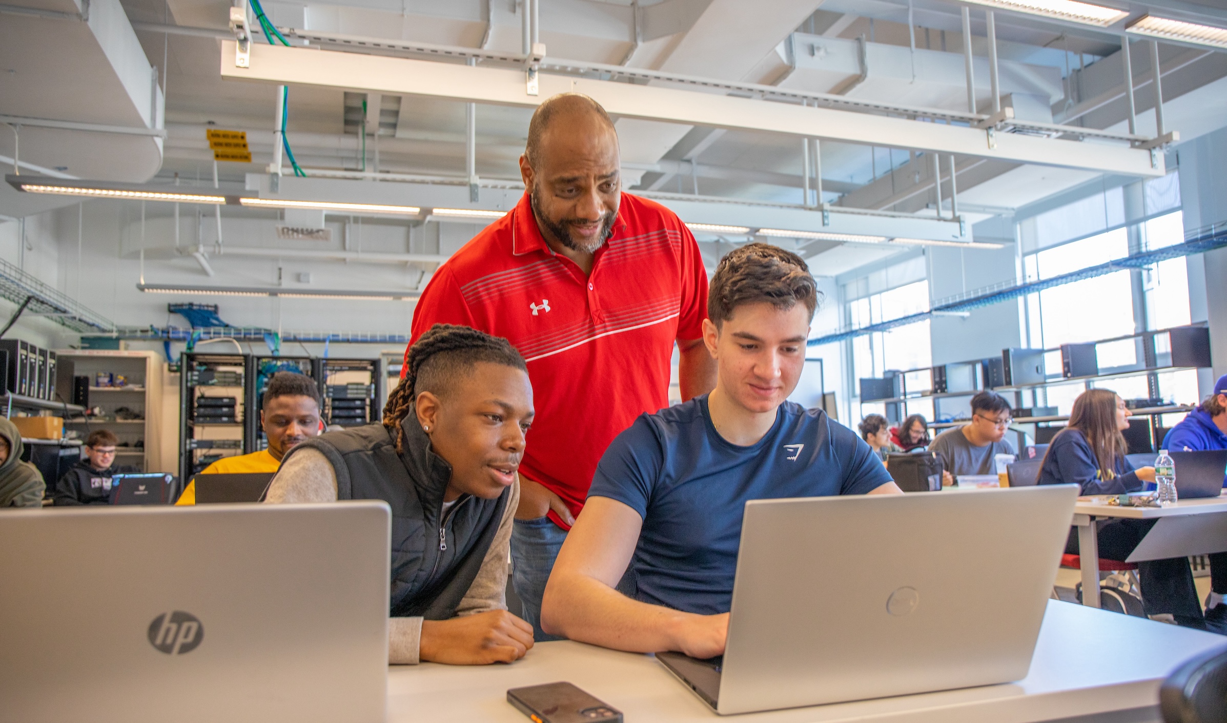 cybersecurity professor helping two JWU students on laptops in cybersecurity lab