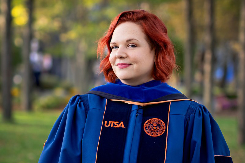 A person standing for a photo with a graduation gown on.