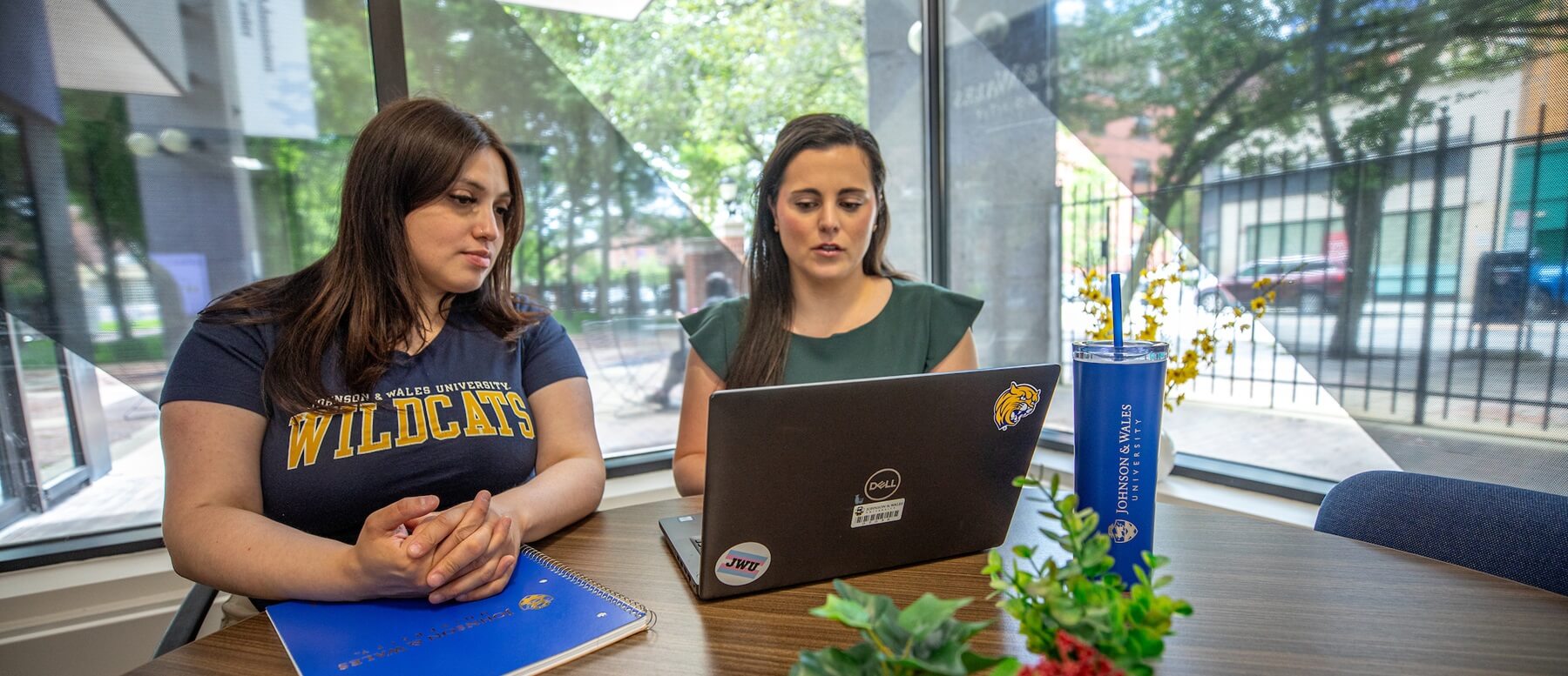 Two JWU Providence students working at a single laptop, with Downcity in the background.