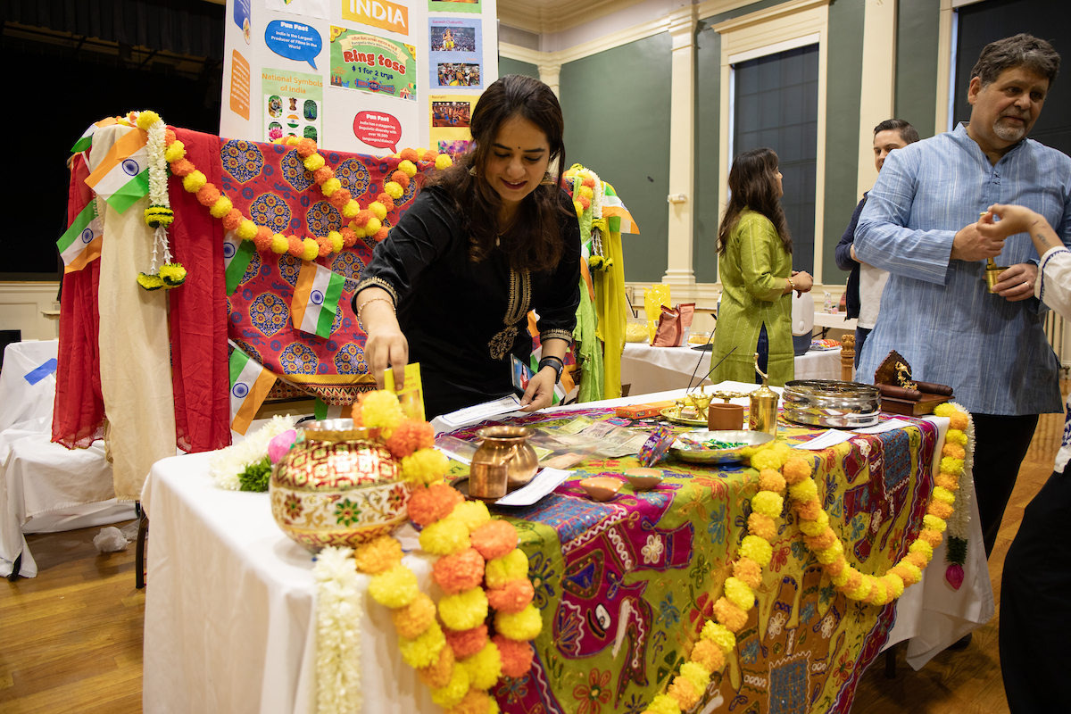 A person interacts with a vibrantly decorated cultural display featuring Indian flags, marigold garlands, and traditional items at an event.