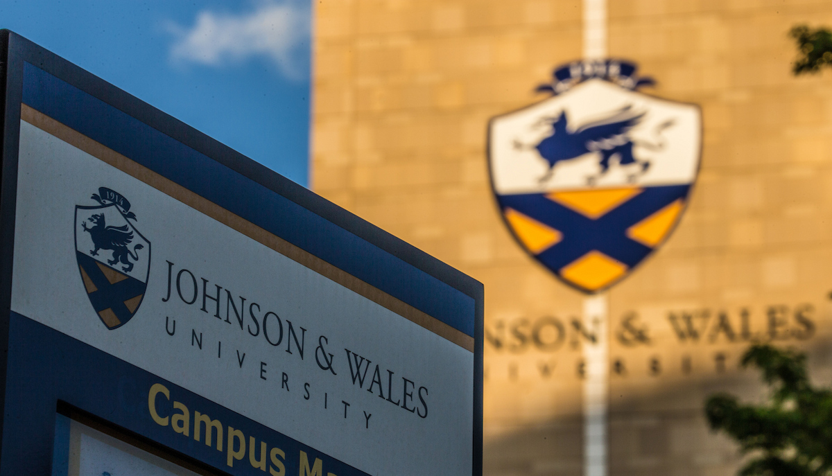 A sign for Johnson & Wales University is prominently displayed in the foreground, with the university's shield emblem visible on a building in the background.