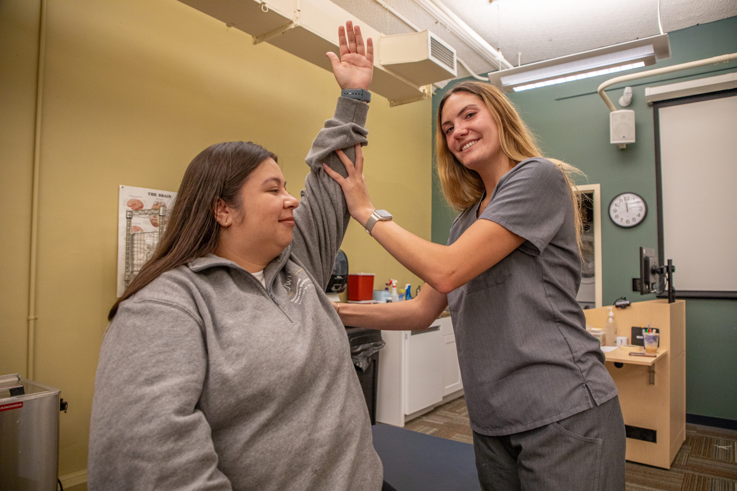 A healthcare professional assists a patient in raising their arm during a clinical examination.