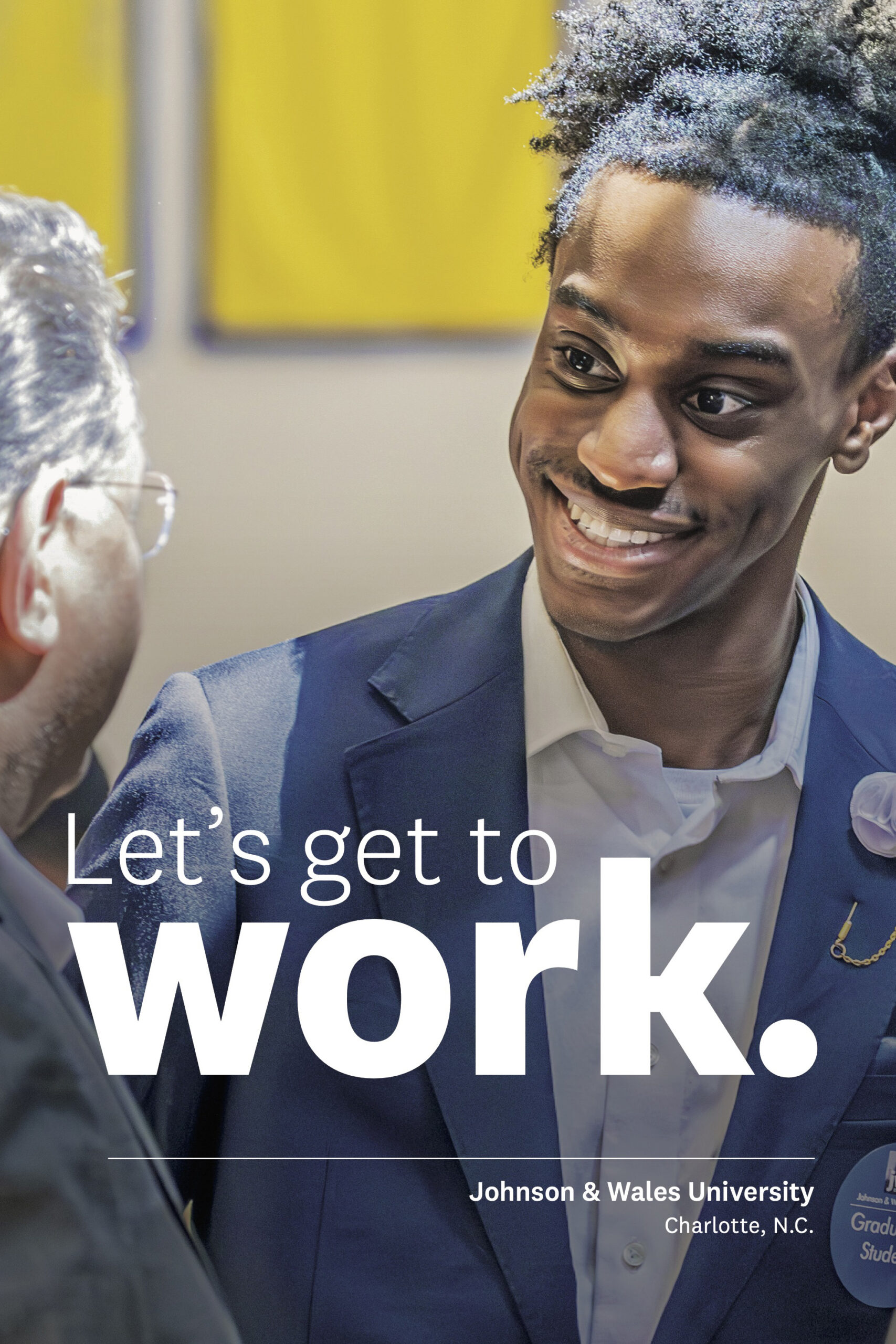 A smiling student in a navy suit and white shirt speaks with another person at Johnson & Wales University in Charlotte, N.C. The graphic includes the text “Let’s get to work” and the university name and location.