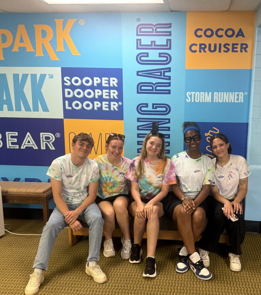 Five people sitting on a bench in front of a colorful background.