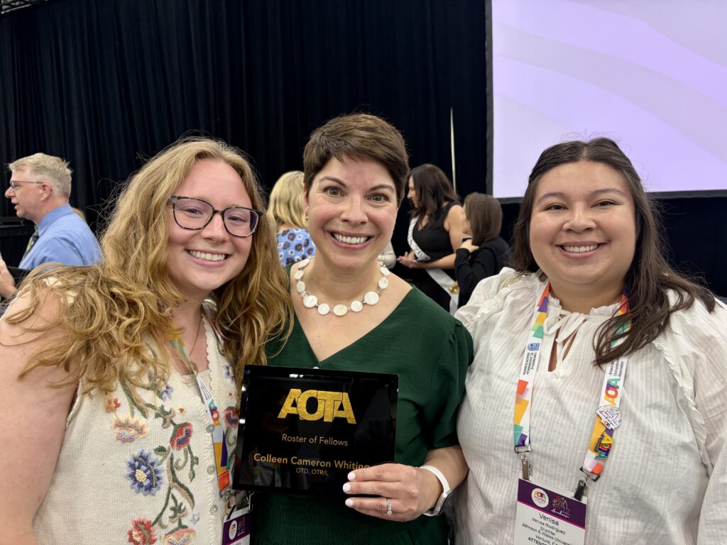 three women pose together smiling, with one holding up an AOTA award