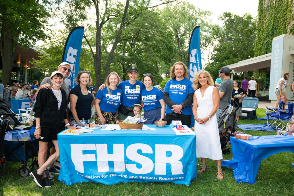 FHSR staff and volunteers gather around a table smiling at their yearly event in August for their Music to My Ears program