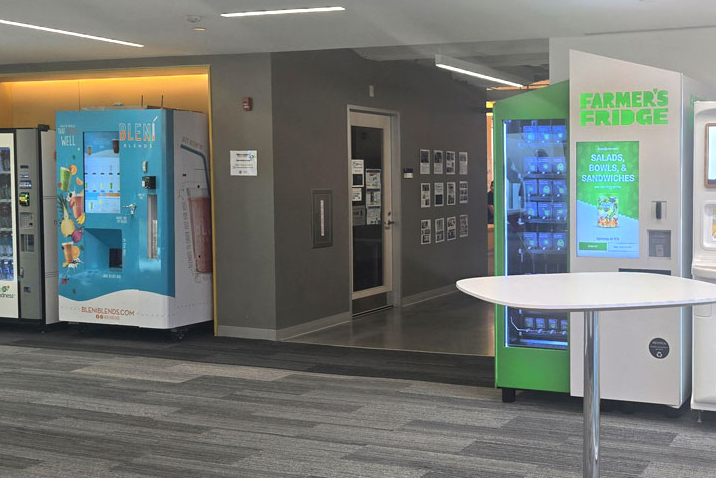 A lounge area with several vending machines, including a blue Blend vending machine and a green Farmer’s Fridge machine offering salads, bowls, and sandwiches.