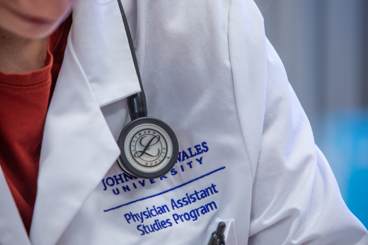 A person wearing a white lab coat with "Johns Hopkins University Physician Assistant Studies Program" embroidered on it, and a stethoscope hanging around their neck.