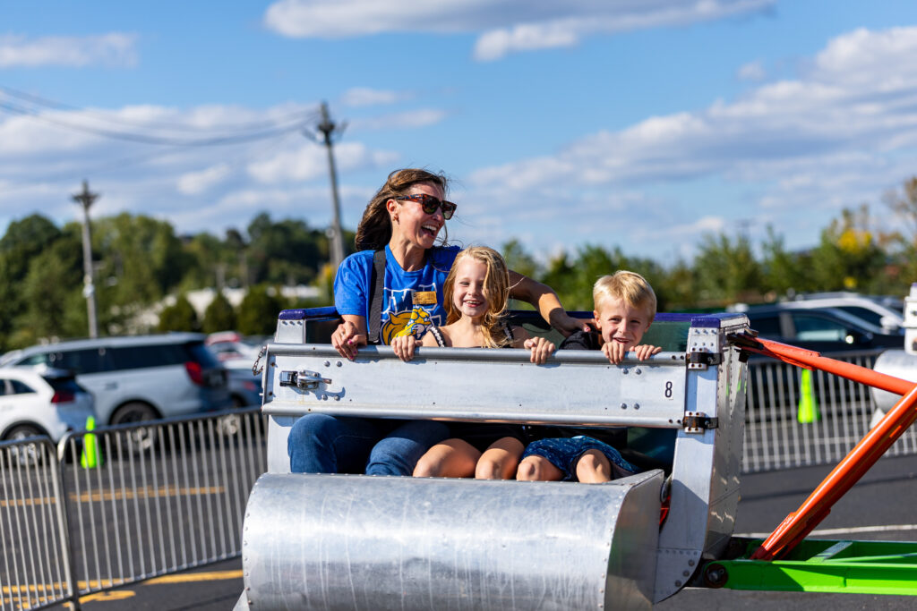 A family of three enjoys a ride on a metal amusement park attraction under a bright blue sky.
